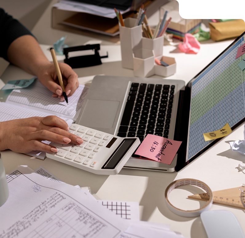 Person surrounded by paperwork, calculator, and spreadsheets, symbolizing manual repetitive work that can be automated